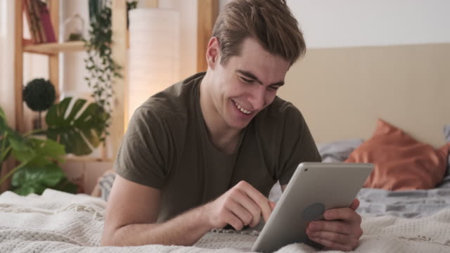 Glücklicher-Mann-mit-digitalen-Tablet-im-Bett