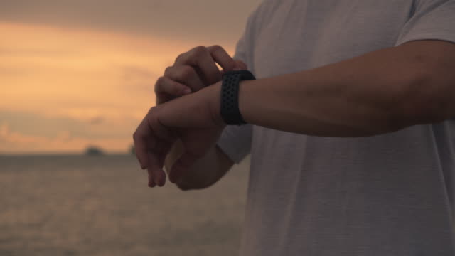 Close-up-Asian-athlete-runner-checking-heart-rate-on-smartwatch-after-running-while-standing-on-the-beach-during-a-beautiful-sunset-in-summer.