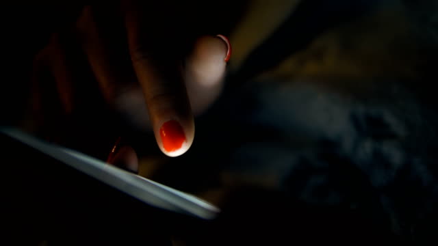 Mujer-usando-una-tableta-en-la-oscuridad-navegando-por-la-pantalla-táctil-azul-brillante-con-el-dedo,-con-el-espacio-de-copia