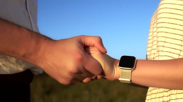 Close-up-of-caucasian-couple's-hand-in-hand-who-stand-in-a-summer-field-in-slowmo