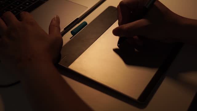 Vista-de-cerca-de-la-mano-del-diseñador-gráfico-usando-la-tableta-gráfica-trabajando-durante-la-noche