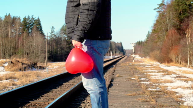 Hombre-con-globo-en-forma-de-corazón-rojo-cerca-del-ferrocarril
