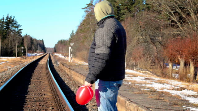 Hombre-con-globo-rojo-en-forma-de-corazón-cerca-de-ferrocarril-en-invierno