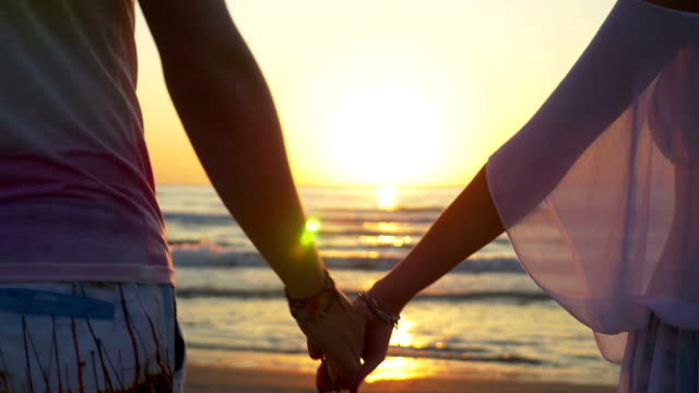 Romantic-couple-holding-hands-and-walking-towards-the-water-on-sandy-beach