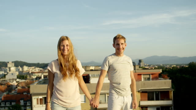 CLOSE-UP:-Happy-man-and-smiling-woman-standing-on-rooftop-raising-hands