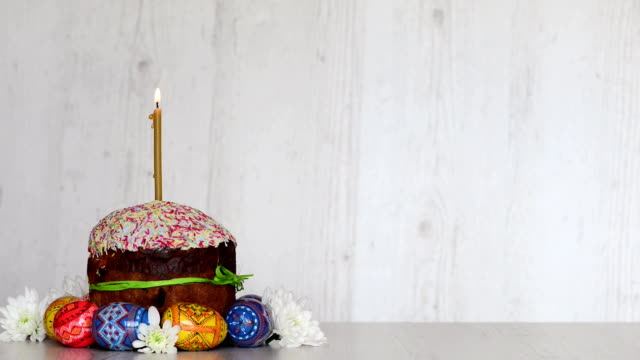 Easter-cake-kulich-with-candle-and-eggs-at-spring-flowers-on-light-wooden-background