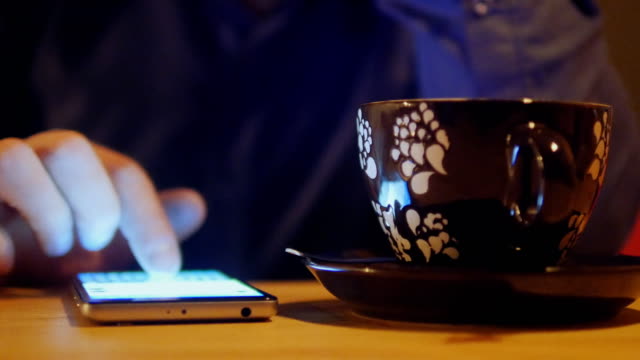 Close-up-of-man-hands-using-smartphone-for-messaging.-The-phone-rests-on-a-table-and-is-next-to-a-cup-of-coffee.