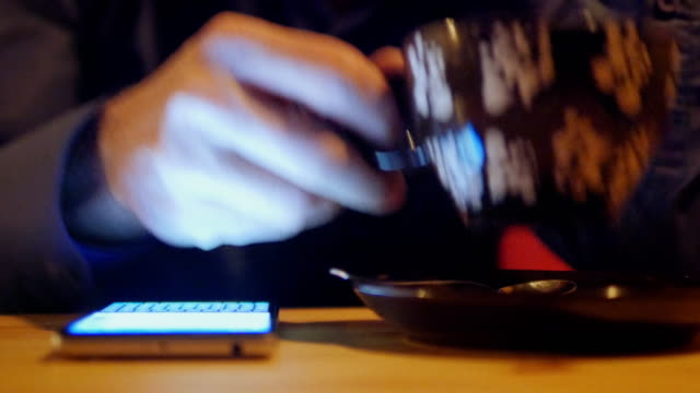 Close-up-of-man-hands-using-smartphone-for-messaging.-The-phone-rests-on-a-table-and-is-next-to-a-cup-of-coffee.-Man-drinks-coffee-and-chatting.