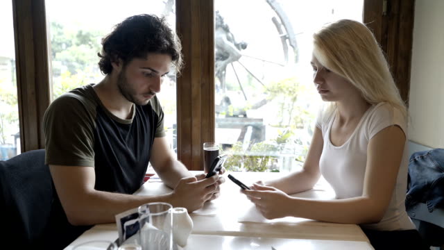 Teen-Paar-mit-Beziehungsprobleme-Vernetzung-in-sozialen-Netzwerken-mit-Smartphones-sitzt-am-Tisch-im-restaurant
