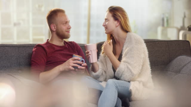 Young-boyfriend-removing-a-wisp-from-his-girlfriend-while-drinking-tea-on-a-couch