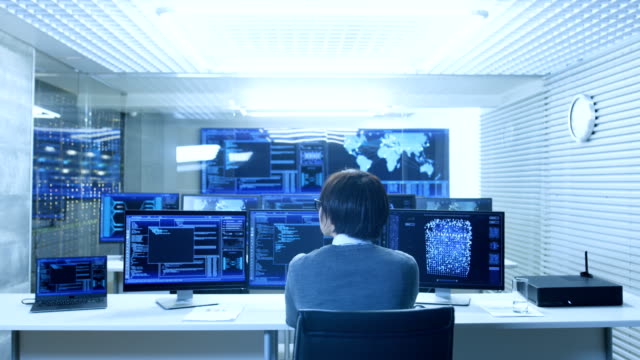 In-the-System-Control-Monitoring-Room-Operator-Works-with-Multiple-Displays-Showing-Graphics,-Logistics,-Neural-Networks.-Data-Center-is-Light-and-Full-of-Advanced-Technologies.