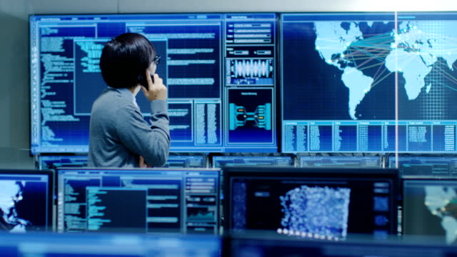 In-the-System-Control-Room-IT-Administrator-Talks-on-the-Phone.-He's-in-a-High-Tech-Facility-That-Works-on-the-Surveillance,-Neural-Networks,-Data-Mining,-AI-Projects.