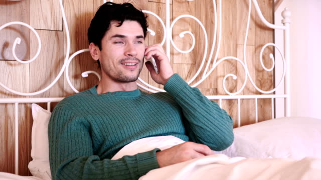 Man-Sitting-in-Bed-Dialing-call-and-Talking-on-Phone