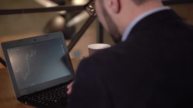 Mann-in-Gläser-Studien-Handel-Grafik-auf-einem-Laptop-in-einem-Café-sitzend