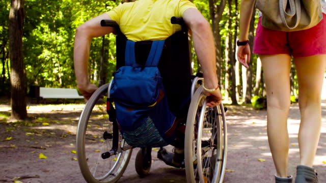 Wheels-of-a-wheelchair-and-woman's-legs-during-the-walk