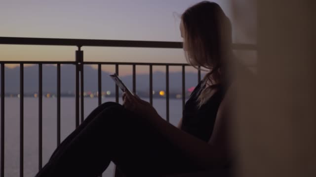 Frau-mit-Smartphone-auf-dem-Balkon-mit-Blick-auf-Meer