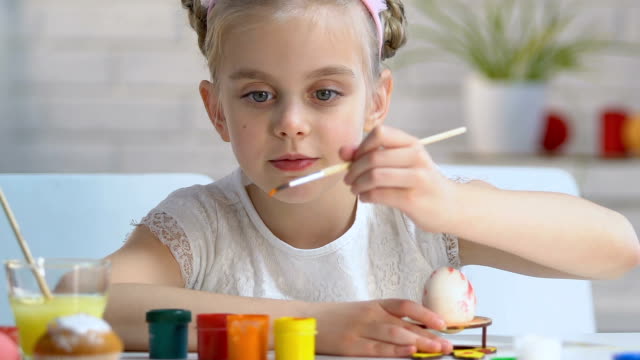 Diligent-girl-carefully-putting-pattern-with-paints-on-egg,-Easter-decoration