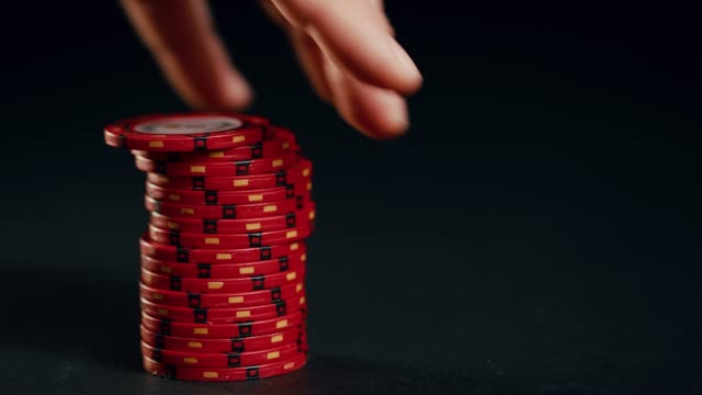 A-stack-of-red-poker-chips-slides-in-on-a-black-background.-At-the-end-the-hand-takes-them-away.
