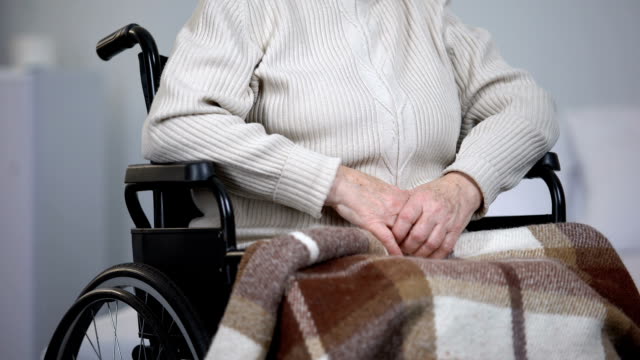 Anciana-en-silla-de-ruedas-limpiando-las-lágrimas-de-la-cara-y-mirando-a-cámara,-soledad