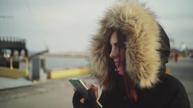 Nahaufnahme-Schuss-der-schönen-Frau-mit-Smartphone-Technologie-App-zu-Fuß-auf-der-Straße-in-einer-warmen-Jacke-mit-einer-flauschigen-Kapuze