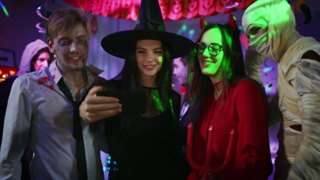 Fiesta-de-disfraces-de-Halloween:-cerebro-muerto-Zombie,-sangre-sediento-de-Drácula,-venda-de-la-momia-hermosa-bruja-y-seductora-ella-diablo-posando-para-grupo-video-Selfie-tomada-con-smartphone.-Los-monstruos-se-divierten
