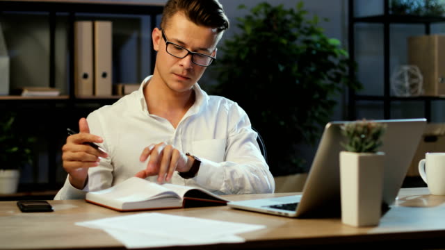 Junge-Geschäftsleute,-die-Laptop-verwenden,-notieren-etwas-im-Notizbuch,-während-sie-am-Abend-im-Büro-arbeiten.