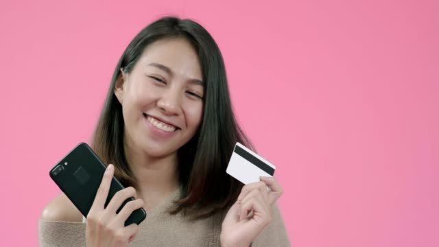 Junge-asiatische-Frau,-die-Smartphone-kauft-Online-Shopping-per-Kreditkarte-Gefühl-glücklich-lächelnd-in-lässiger-Kleidung-über-rosa-Hintergrund-Studio-Shot.-Glücklich-lächelnde-entzückende-Frau-freut-sich-über-Erfolg.