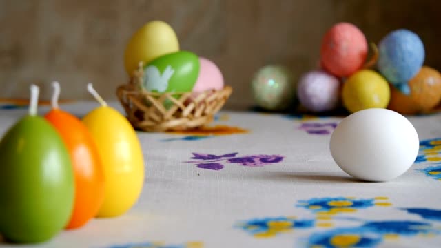 Frohe-Ostern.-Weibliche-Hand-legt-auf-den-Tisch-zwei-Ostereier.-Bunte-Kerzen-und-bunte-Ostereier-im-Hintergrund.