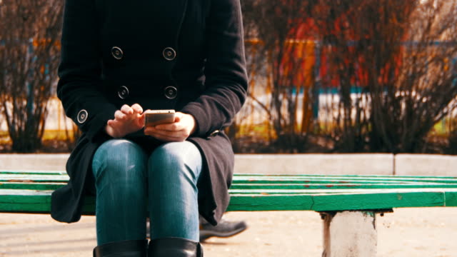 Mädchen-mit-einem-Handy-auf-einer-Bank-im-Stadtpark-im-Frühjahr
