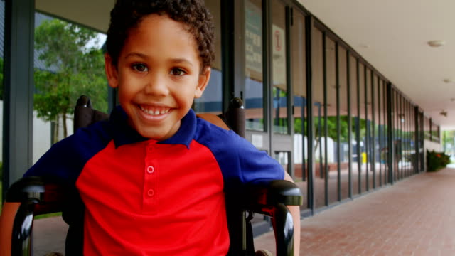 Front-view-of-happy-disabled-African-American-schoolboy-sitting-on-wheelchair-in-school-corridor-4k