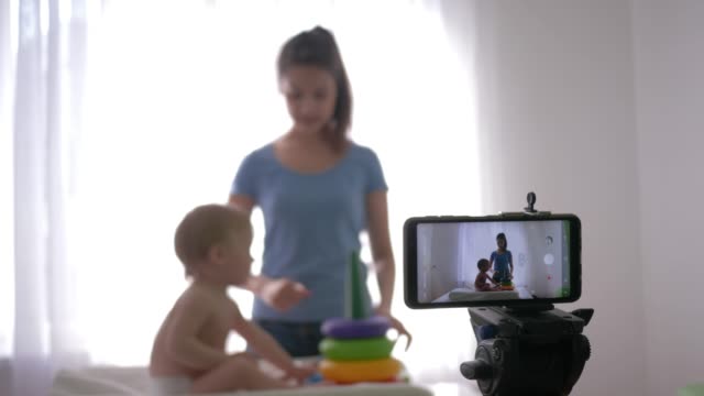 Blog-Aufzucht-Kind,-junge-Mutter-Blogger-mit-Kind-spielt-die-Entwicklung-von-Spielzeug,-während-die-Aufnahme-von-Live-Tutorial-Video-auf-Smartphone-für-Abonnenten-in-sozialen-Netzwerken