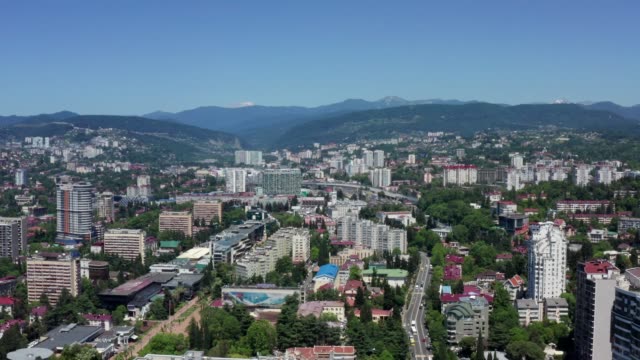Aerial-video-shooting.-Panoramic-view-of-the-city-center-of-Sochi.-High-building-on-a-background-of-green-mountains.-No-people.-Blue-clear-sky.-camera's-moving-forward.