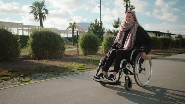Glückliche-junge-Rollstuhlfahrerin-geht-an-sonnigem-Tag-im-Park