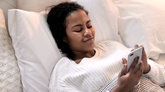 Top-View-of-African-Woman-Using-Smartphone-while-Relaxing-in-Bed