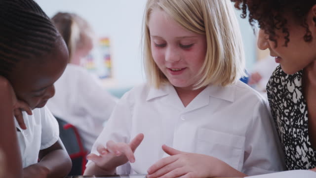 Lehrerin-mit-zwei-Grundschülern,-die-Uniform-mit-digitalem-Tablet-am-Schreibtisch-tragen