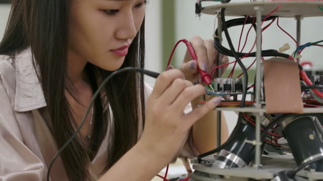 Asian-female-electronics-engineer-works-with-robot,-building,-fixing-robotics-in-workshop.-People-with-technology-or-innovation-concept.