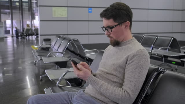 Man-is-scrolling-screen-of-smartphone-in-departure-lounge