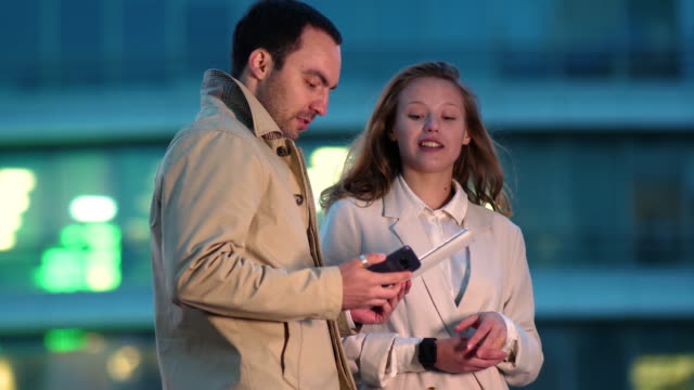 Zwei-junge-Arbeitskollegen,-die-ein-digitales-Tablet-nutzen,-während-sie-spät-in-der-Nacht-draußen-stehen