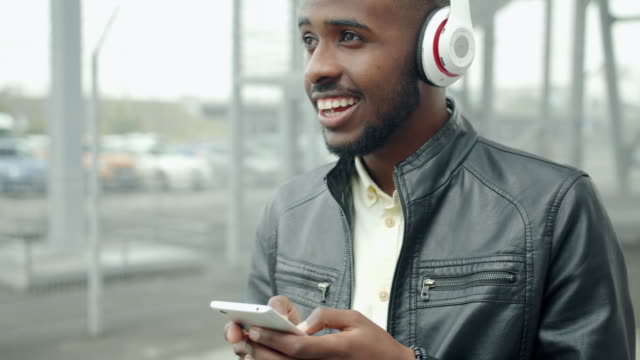 Handsome-guy-in-headphones-using-smartphone-laughing-in-city-street