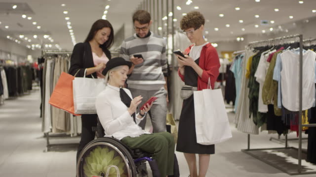 Diverse-Group-of-Friends-Looking-at-Phone-in-Clothes-Store