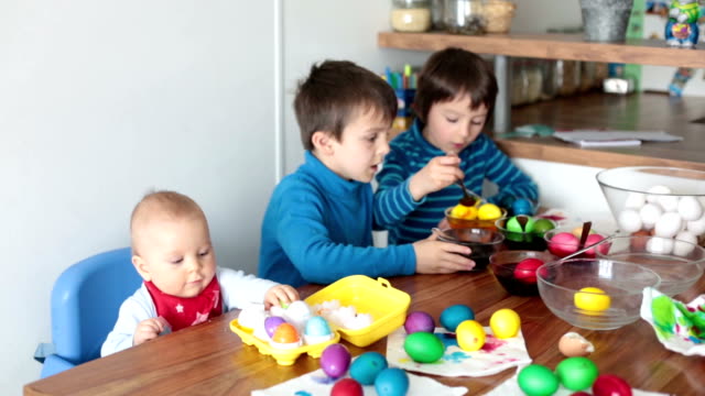 Three-children,-coloring-and-painting-easter-eggs-at-home-for-the-holiday