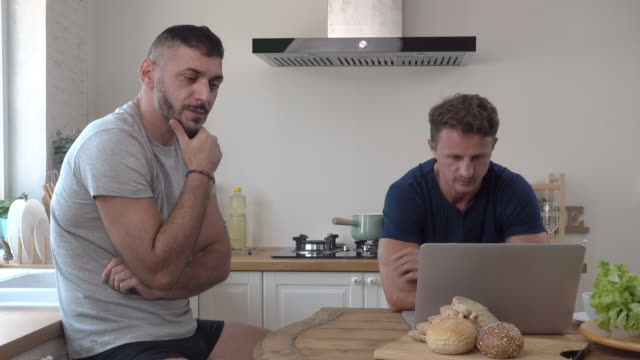 Gay-male-couple-acting-concerned-impatient-and-frustrated-at-kitchen-table