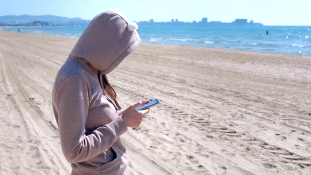 Mujer-irreconocible-está-escribiendo-por-teléfono-en-la-playa-por-mar.