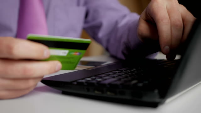 Un-hombre-de-negocios-con-camisa-y-corbata-morada-está-haciendo-un-pago-a-la-banca-por-Internet.-Compras-en-línea-con-tarjeta-de-crédito-en-el-ordenador-portátil.