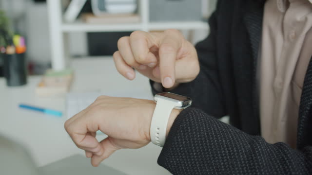 Close-up-of-male-hand-touching-electronic-watch-screen-using-modern-device-in-office