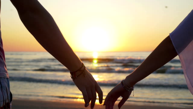 Young-couple-holding-hands-on-the-beach-at-sunset
