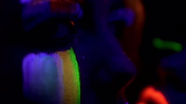 Closeup-view-of-two-beautiful-girls-with-fluorescent-makeup-under-UV-black-light-petting-each-other-and-kissing.-Slowmotion-shot