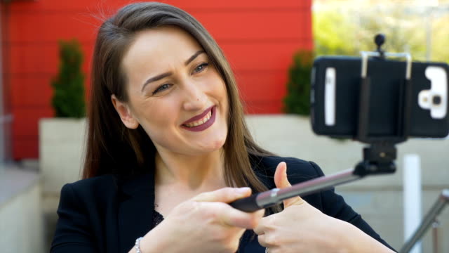 Closeup-view-of-nice-girl-poses-and-makes-funny-faces-with-smartphone-camera-and-selfie-stick-in-the-city