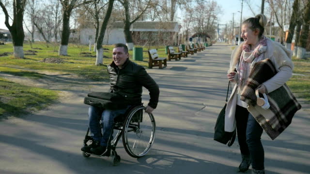Disabeld-man-in-wheelchair-and-girl-walk-along-embankment-smiling,-laughing,-and-talking