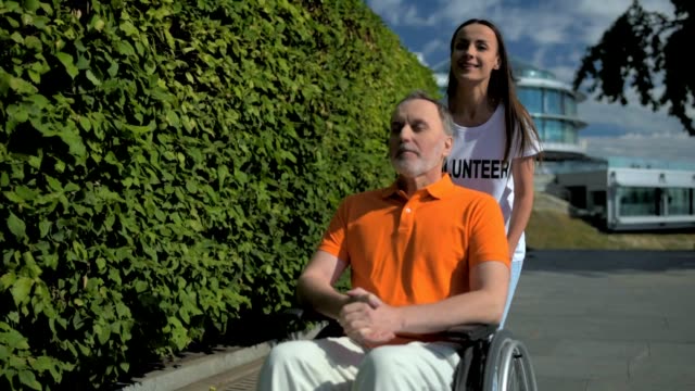 Positiven-weiblichen-Freiwilligen-drücken-einen-wheelchaired-Mann